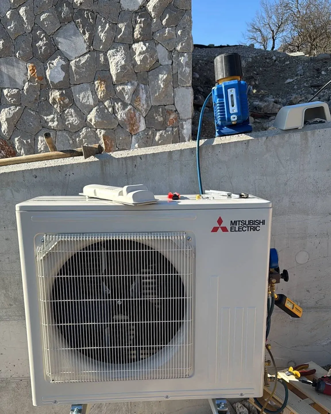 Zunanja enota Mitsubishi Electric na nosilcu ob kamnitem zidu med montažo